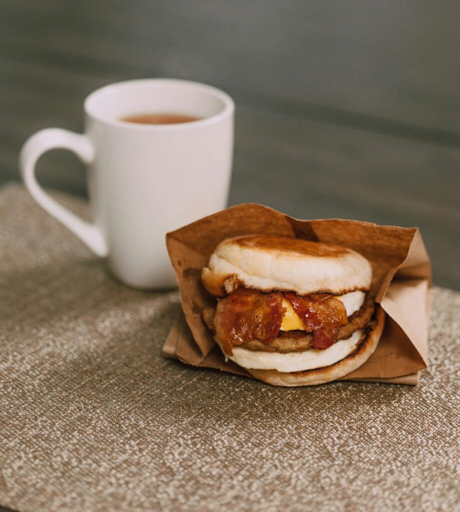 Appetizing breakfast sandwich paired with a steaming cup of coffee on a rustic table.