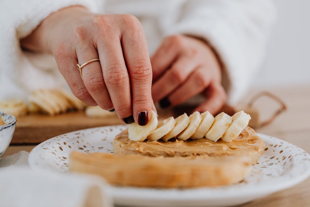 A hand places banana slices on peanut butter toast, highlighting a healthy snack preparation.