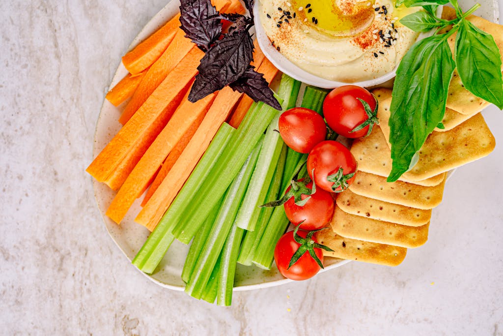 Top view of a fresh vegetable and hummus platter with carrots, celery, cherry tomatoes, and crackers.
