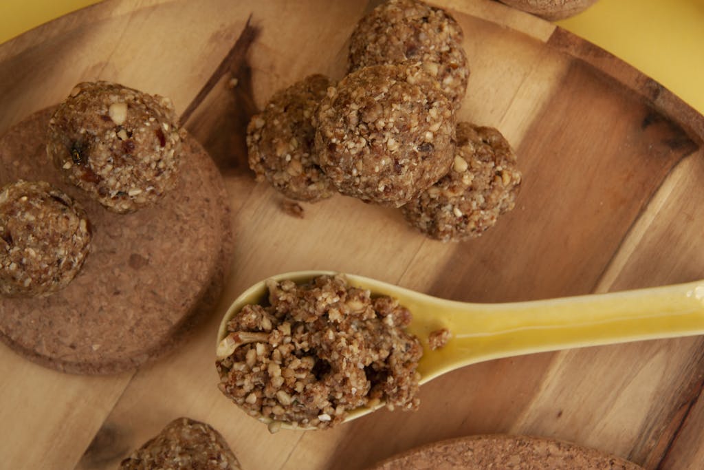 Top view of homemade nut energy bites served on a wooden tray with a yellow spoon for healthy snack options.